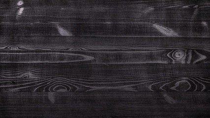 Black rustic wooden table background with a distinct texture of wood fibers and knots with...