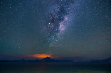 Wide landscape at night on the shore of Lake Llanquihue. The Milky Way passing through the Osorno and Calbuco volcanoes