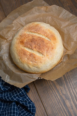 Round Loaf of Freshly Baked Sourdough Bread on Parchment Paper on Wood Table