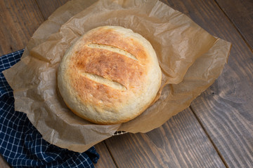 Round Loaf of Freshly Baked Sourdough Bread on Parchment Paper on Wood Table