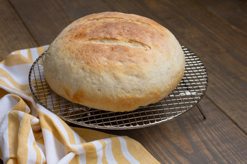 Round Loaf of Freshly Baked Sourdough Bread on Cooling Rack on Wood Table with Yellow and White Kitchen Towel