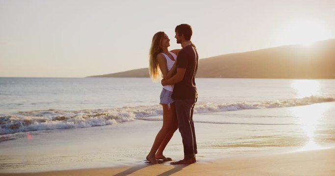 Young attractive couple embracing and kissing on the beach at sunset in slow motion, summer romance