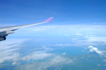 Wing of airplane above the sky over a cloudscape, natural green island and blue ocean