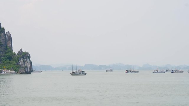 Ship cruising in Halong Bay while other boats are anchored with misty horizon
