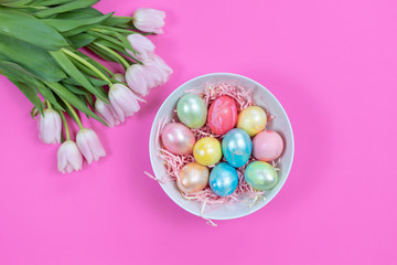 Bright colorful Easter eggs and fresh tulips on pink background