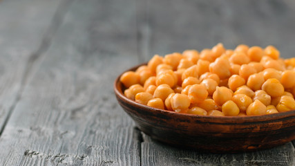 A clay bowl filled with boiled chickpeas on a black wooden table.