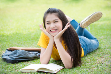 Pretty Asian female teenager smiling while lying on grass field in park