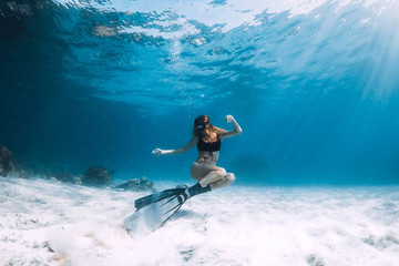 Freediver young woman with fins swim over sand in underwater ocean