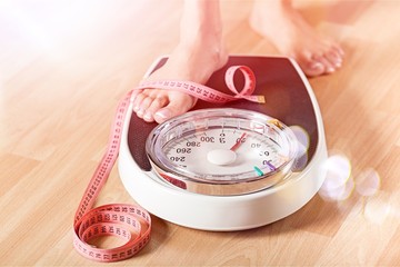 Young woman standing on scales with measuring tape on wooden background