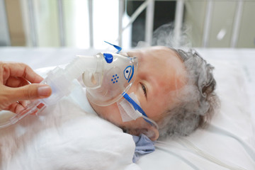 Toddler boy using nebulizer to cure asthma or pneumonia disease . Sick baby boy rest on patients...