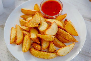 Fried potatoes with red tomato sauce on the white plate.