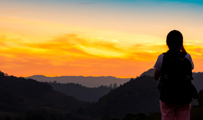 Fototapeta na wymiar Back view of young woman watching beautiful sunset over mountain layer. Backpacker happy in travelling alone. Silhouette of tourist hiking to top of mountain. Adventure activity of active girl.