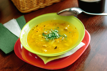 Vegetable soup in a green plate over a wooden table.