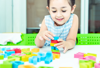 Cute kids female playing with toy designer on the floor at home. Child girl exciting while playing with alphabet colorful blocks. Kindergarten educational games for determination, intention concept
