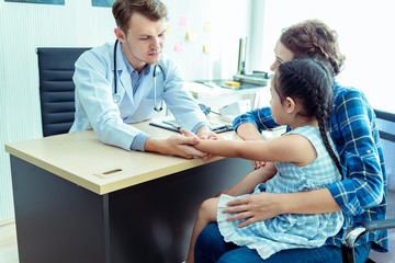 Fototapeta premium Young friendly caucasian pediatrician doctor is examining child patient girl with her mother ,consultation with a stethoscope and tablet pc in clinic office .Healthcare and medical kid concept