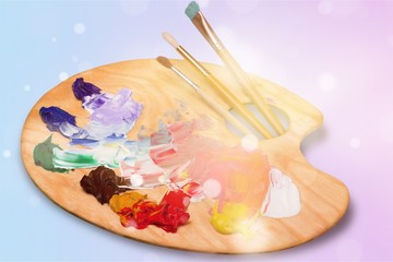 Wooden art palette with blobs of paint and a brushes on white background