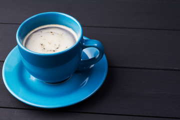 Cafe en taza azul con plato que le hace juego en fondo de madera negra
