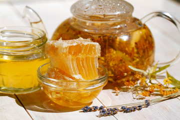 teapot linden lavender tea and flowers on white wooden table with Fresh Honey comb and jar of Delicious fluid honey. close-up shot in bright day sunlight. bee products by organic natural concept.