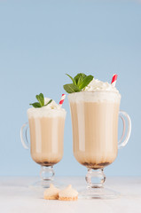 Refreshment coffee drinks with green fresh green mint, whipped cream, red striped straw, cookies in light blue interior on white wood table, vertical.