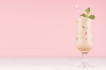Coffee cold alcohol cocktail in goblet with green mint, ice cubes, straw in pastel light pink...