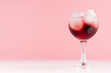 Summer fresh red cocktail in wineglass with blueberry, ice cubes  on white wood table and pastel pink wall, copy space.