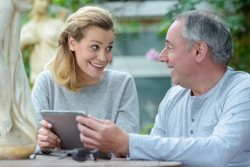 woman and dad sitting in outdoor cafe checking digital tablet