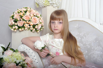 blonde young princess sits in a white smart dress on the couch among the flowers