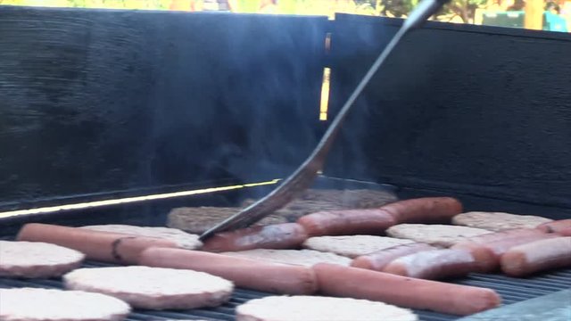 Burgers and Hot dogs being cooked and flipped on a grill.