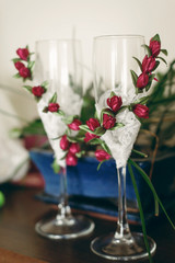 Two empty champagne glasses decorated with white lace and red roses flowers on hotel room table, morning wedding preparation
