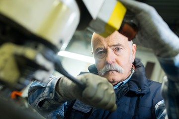 senior mechanic working on car with open bonnet
