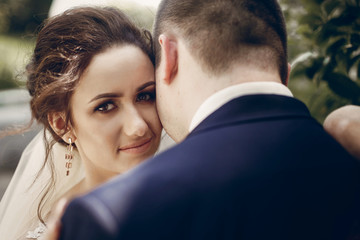 Beautiful brunette bride portrait face close-up, sensual groom kissing hugging bride, newlywed couple posing outdoors in park afrer wedding ceremony