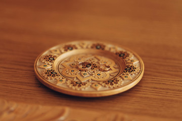 Two golden wedding rings on rustic wooden plate with embroidery on table close-up, couple of gold engagement rings in wedding registry office, marriage concept