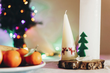 christmas rustic table with candle with reindeers and felt tree and fruits on colorful lights background. space for text. seasonal greetings holidays card concept