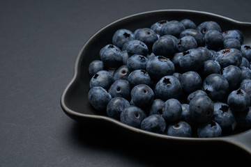 Blueberries on a black clay pan with black background, closeup view.
