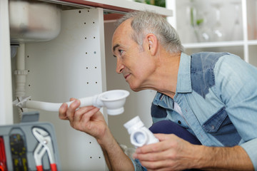 senior citizen using pipe wrench to tighten-up pipes under sink