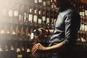 Male sommelier pouring red wine into long-stemmed wineglasses. Waiter with bottle of alcohol beverage.