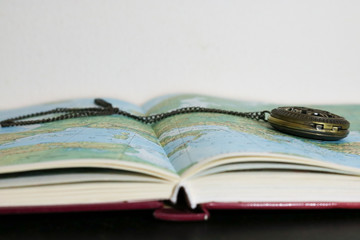 Primo piano di un atlante e orologio da taschino vintage, viaggi e geografia © Sara