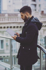 Young stylish man reading book holding tablet pc in a city