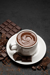 Cup of hot chocolate and pieces of chocolat on dark concrete background