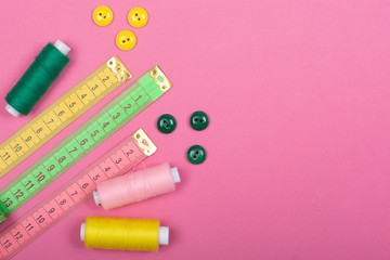Tailoring. Sewing supplies and accessories for sewing and needlework. Centimeter, buttons and coils with threads of green, pink and yellow on a pink background. Flat Lay, Copy space