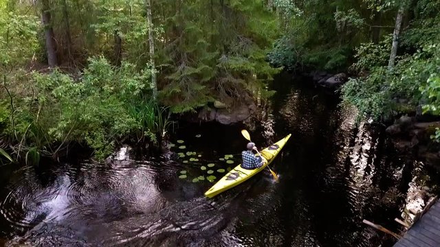 Aerial, rising, drone shot, of a man kayaking, on lake Saimaa, surrounded by green forest, on a sunny, summer evening, in Karjala, Finland
