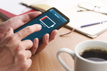 Low battery alert on smartphone screen.Closeup of male hands touching smartphone screen at table.