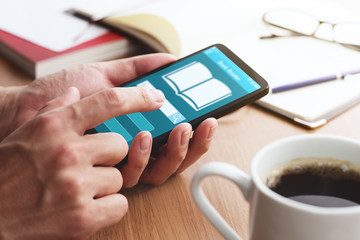 Closeup of male hands touching smartphone screen for reading books at table. Online book reader app on smartphone screen.