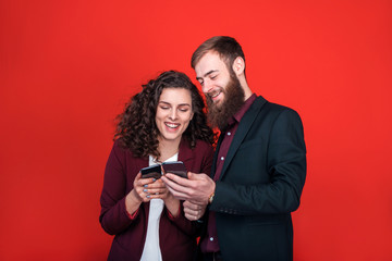 Businessman and businesswoman with gadgets isolated on red background.