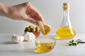 Woman dipping fresh bread into tasty olive oil in bowl