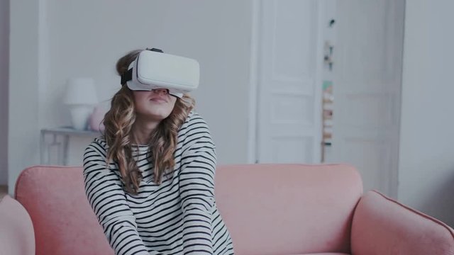 Beautiful brunette girl uses a virtual reality glasses indoors. She is very enthusiastic and moving her hands in the air. Orientation in space using modern vr technology. Future is today.