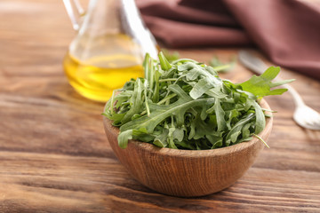 Bowl with tasty fresh arugula on wooden table