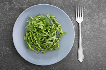 Plate with tasty fresh arugula on grey table