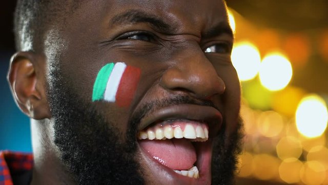 Afro-American sports fan rejoicing favorite team victory, Italian flag on cheek