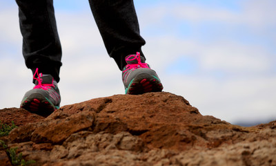 Feet in bright sneakers on a mountain against a blue sky and clouds. Cropped shot, horizontal, space for text, close-up. Tourism concept